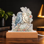 Lovebirds — dusty blue and cream, beaks touching over a wildflower base