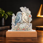 Lovebirds — dusty blue and cream, beaks touching over a wildflower base