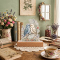 Lovebirds — dusty blue and cream, beaks touching over a wildflower base